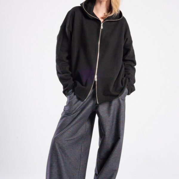 Modelka w bluzie Niigata Black od delCane, cała sylwetka przodem, ręce w kieszeniach spodni, widoczny suwak bluzy rozpinany także od dołu.