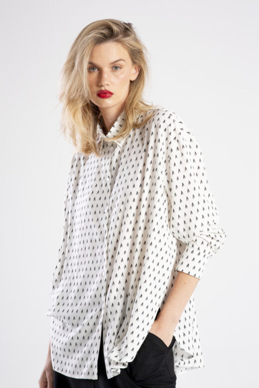 Modelka w koszuli Niigata White od delCane, ujęcie od tyłu, widoczna cała sylwetka. Koszula z włoskiej wiskozy w drobny czarny wzór, o luźnym kroju oversize i zaokrąglonym, lekko dłuższym tyle.