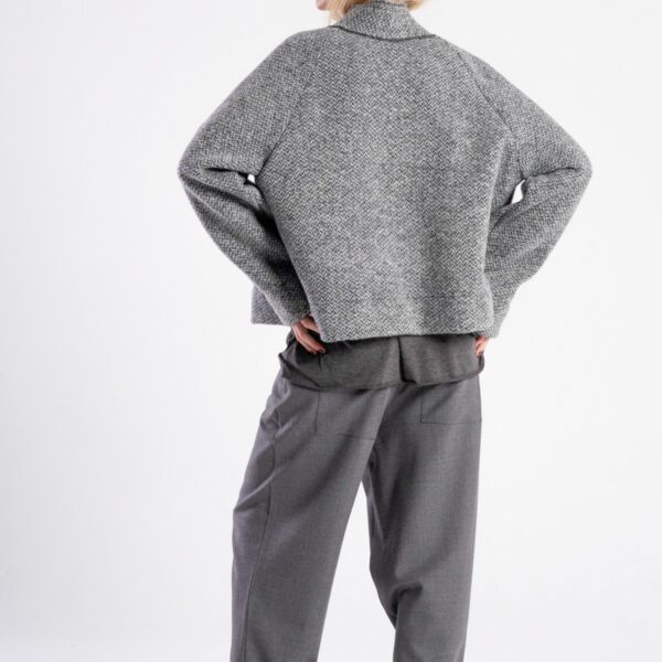 Modelka w kurtce Niigata Grey od delCane, widok z tyłu z lekko widocznym profilem, ręce na biodrach.