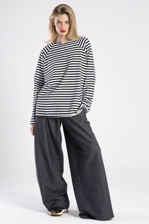 Modelka w longsleeve’ie Niigata Stripes od delCane, cała sylwetka przodem, jedna ręka w kieszeni spodni, druga opuszczona.