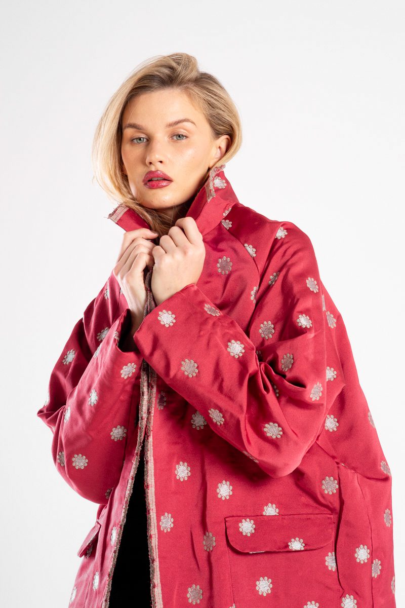Modelka w marynarce Niigata Red od delCane, ujęcie w mocnym zbliżeniu z lekkiego boku, widoczna struktura żakardowej tkaniny i wzór.