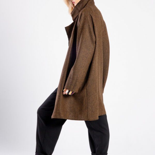 Modelka w płaszczu Niigata Brown & Black od delCane, ujęcie z boku, cała sylwetka, twarz skierowana w bok, ręce luźno opuszczone, jedna noga lekko ugięta.