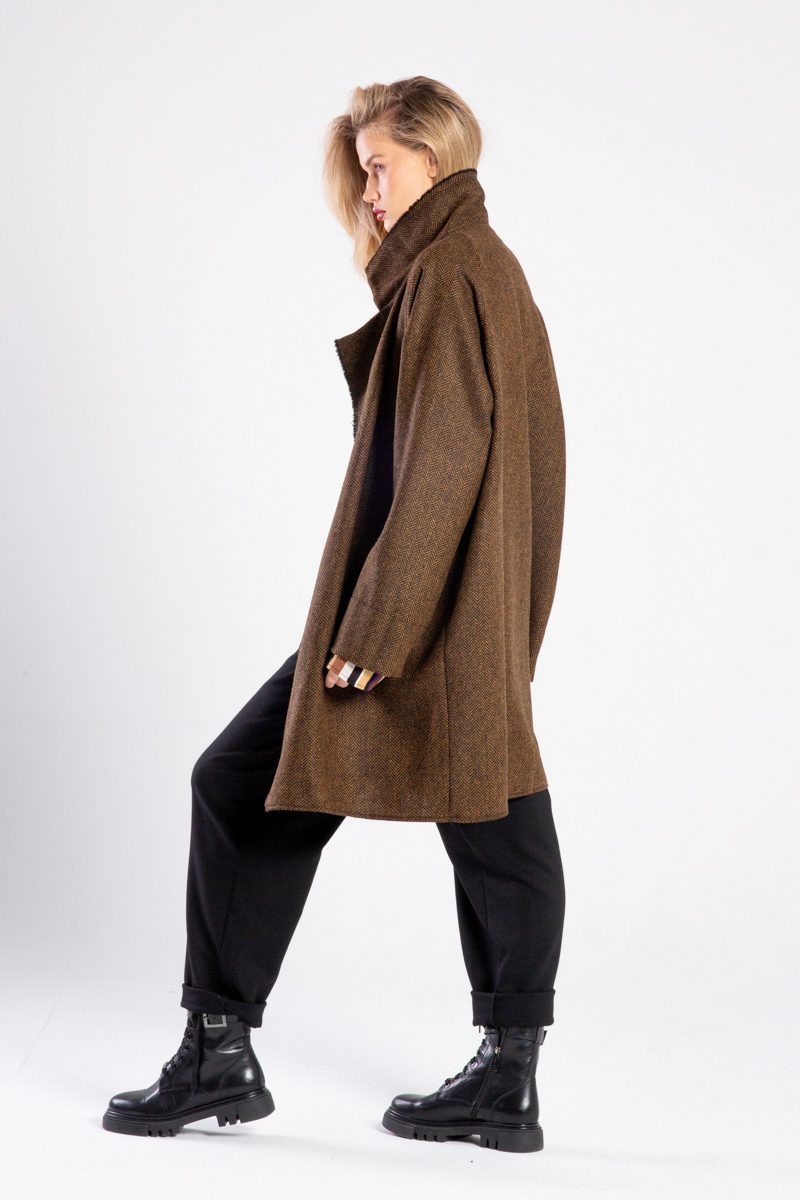 Modelka w płaszczu Niigata Brown & Black od delCane, ujęcie z boku, cała sylwetka, twarz skierowana w bok, ręce luźno opuszczone, jedna noga lekko ugięta.