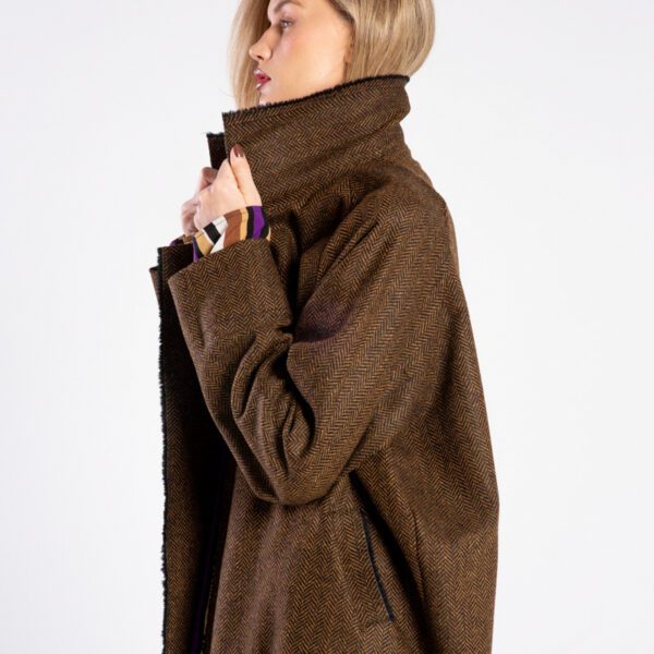 Modelka w płaszczu Niigata Brown & Black od delCane, ujęcie z boku, górna część sylwetki, trzyma kołnierz płaszcza obiema rękami.