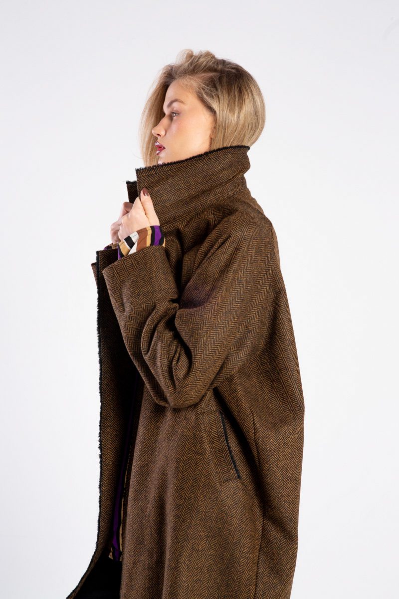 Modelka w płaszczu Niigata Brown & Black od delCane, ujęcie z boku, górna część sylwetki, trzyma kołnierz płaszcza obiema rękami.
