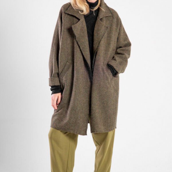 Modelka w płaszczu Niigata Khaki od delCane, widok z przodu, jedna ręka w kieszeni, druga opuszczona, płaszcz luźno.