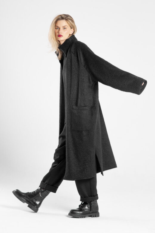 Modelka w płaszczu Niigata Noir od delCane, ujęcie z boku w ruchu, twarz skierowana do przodu.