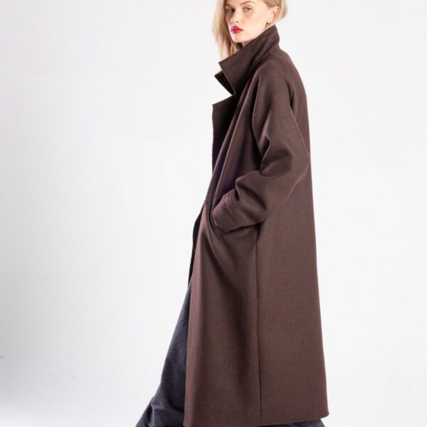 modelka w płaszczu Niigata Brown z wełny, pełna sylwetka bokiem, rozpięty płaszcz, ręce w kieszeniach, patrzy w obiektyw