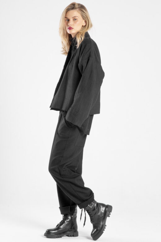 Modelka bokiem, patrzy w obiektyw, jedna noga lekko ugięta, ręka w kieszeni spodni Niigata Black.