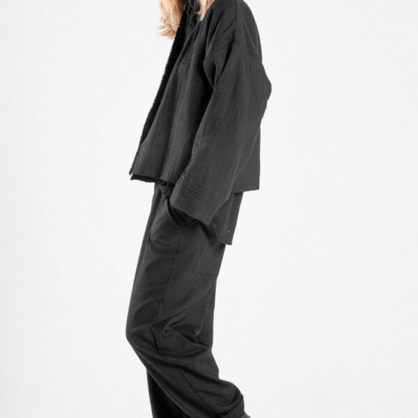 Modelka bokiem, patrzy w obiektyw, jedna noga lekko ugięta, ręka w kieszeni spodni Niigata Black.