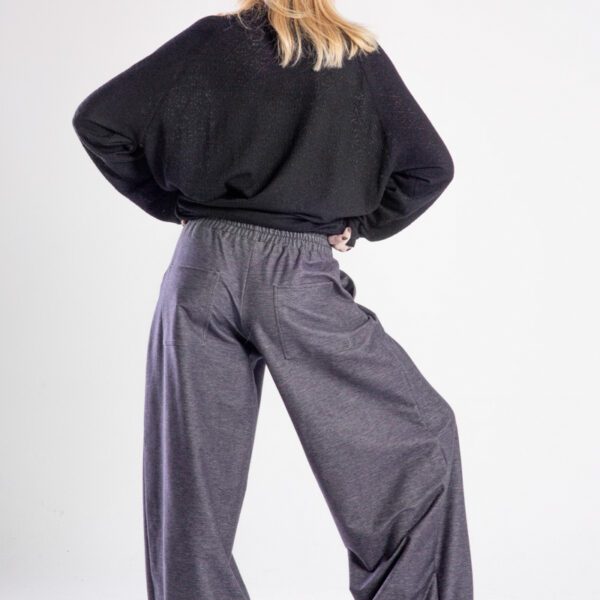 Modelka w spodniach Niigata Jeans od delCane, cała sylwetka tyłem - ręce na biodrach, jedna noga ugięta, widoczne tylne kieszenie.