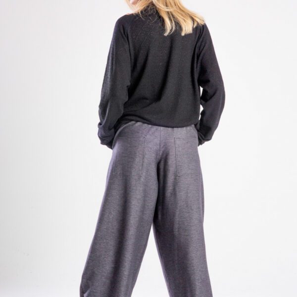 Modelka w spodniach Niigata Jeans od delCane, cała sylwetka tyłem - obie ręce w kieszeniach spodni, widoczny tył.