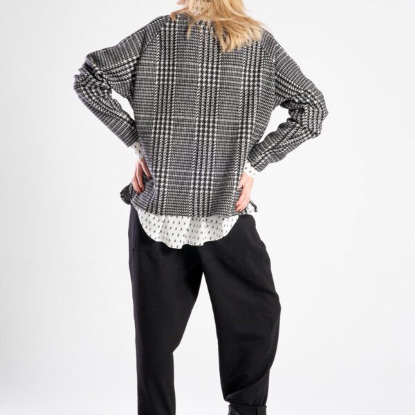 Modelka w swetrze Niigata Black & White od delCane, ujęcie z tyłu, cała sylwetka, ręce ugięte i oparte powyżej bioder.