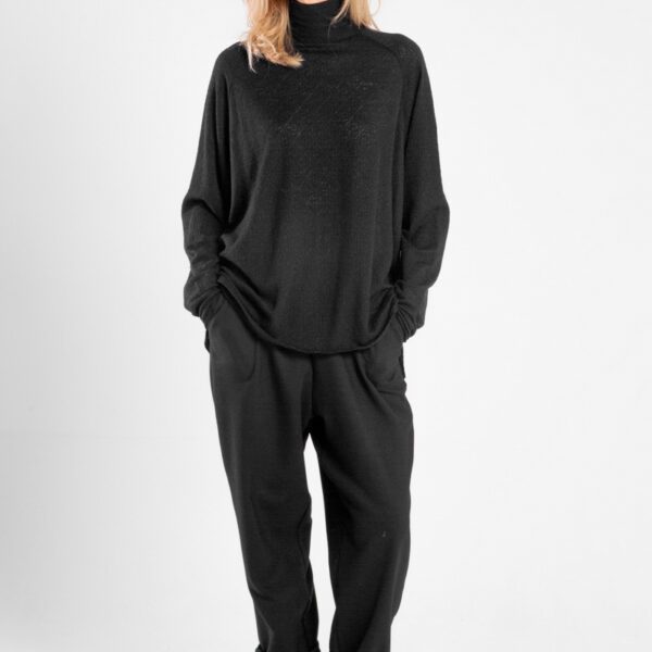 Modelka w czarnym golfie Niigata Cashmere od delCane, widok z przodu z rękami w kieszeniach.
