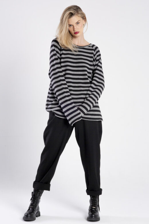 Modelka w swetrze Niigata Stripes od delCane, ujęcie z przodu, cała sylwetka, dłonie splecione z przodu, widoczne długie rękawy swetra.