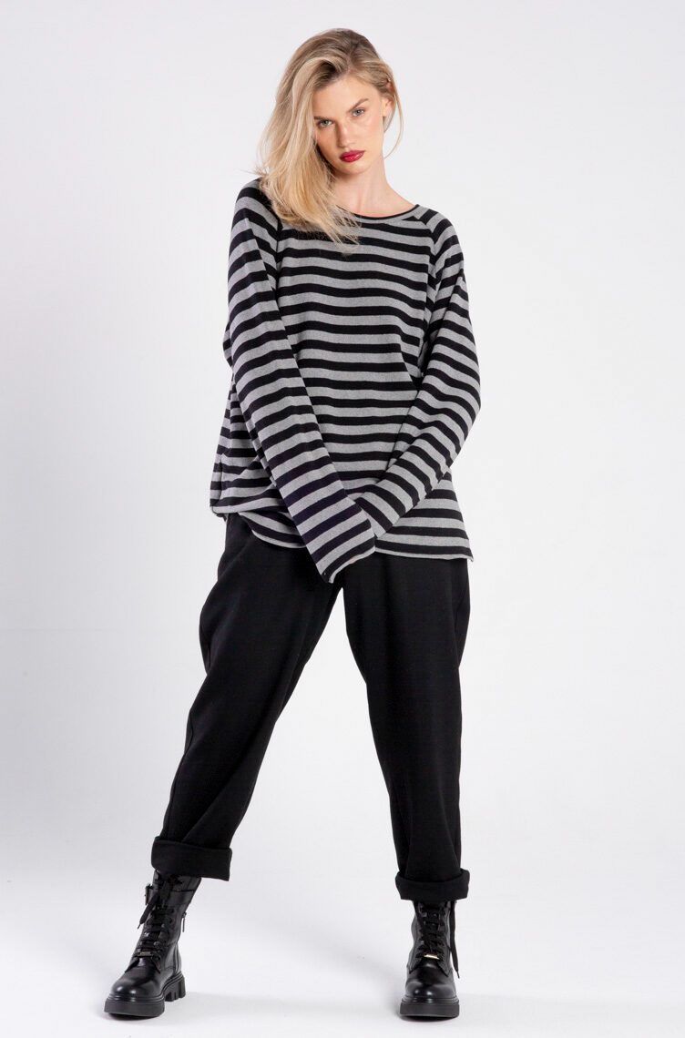 Modelka w swetrze Niigata Stripes od delCane, ujęcie z przodu, cała sylwetka, dłonie splecione z przodu, widoczne długie rękawy swetra.