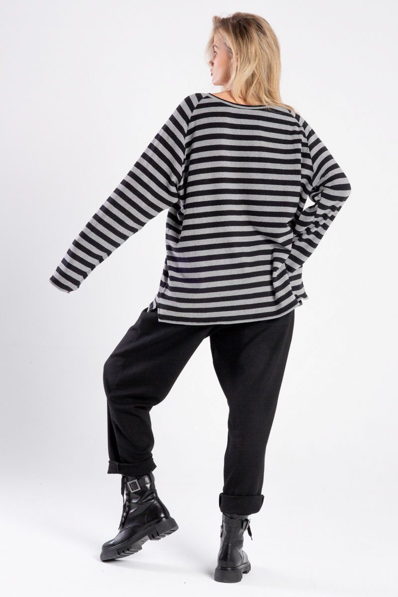 Modelka w swetrze Niigata Stripes od delCane, ujęcie z tyłu, cała sylwetka, jedna ręka oparta na biodrze, ugięta noga, widoczny cały tył swetra.