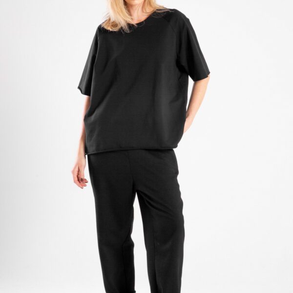 modelka w t-shircie Niigata Black, pełna sylwetka przodem, jedna ręka wzdłuż ciała, druga z tyłu, widoczny przód t-shirtu
