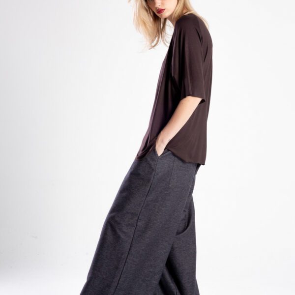 Modelka bokiem w brązowym t-shircie oversize, z wysuniętą nogą i ręką w kieszeni spodni.