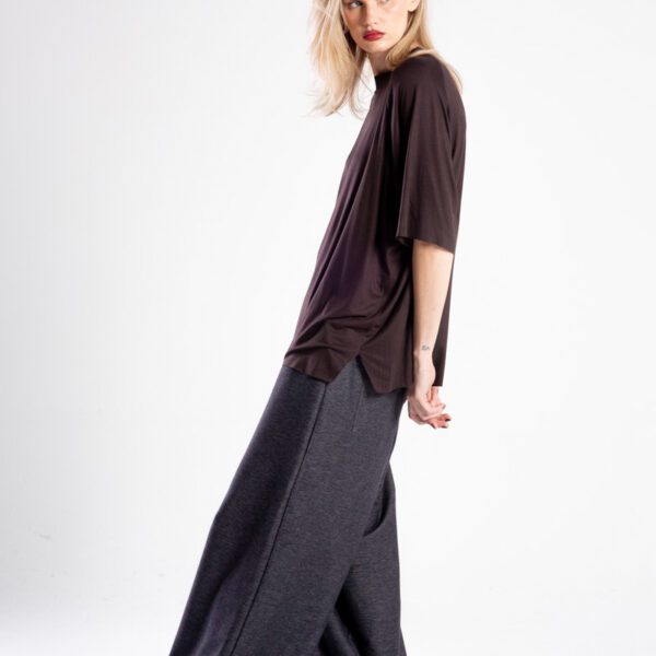 Modelka bokiem w brązowym t-shircie oversize, patrząca przez ramię, widoczne boczne rozcięcie.