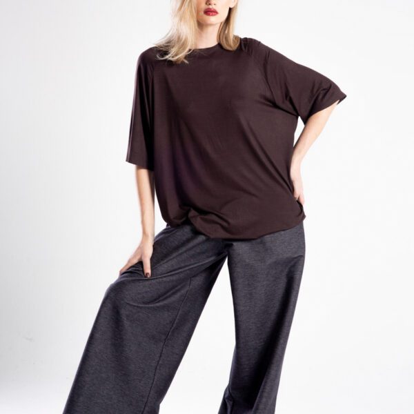Modelka przodem w brązowym t-shircie oversize, cała sylwetka, jedna noga ugięta i ręka oparta na udzie.