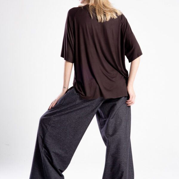 Modelka tyłem w brązowym t-shircie Niigata Brown, cała sylwetka, jedna noga ugięta.