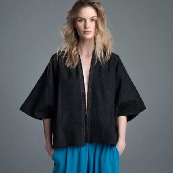 Modelka prezentuje kimono Noda Black w ujęciu od kolan w górę, kimono jest rozwiązane i rozpięte, ręce ma wsunięte w kieszenie spodni, wyraźnie widać jego luźną formę.