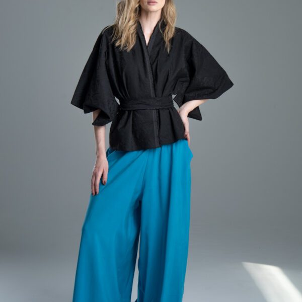 Modelka przodem prezentuje kimono Noda Black w pełnej sylwetce, jedna noga jest lekko ugięta, jedna ręka oparta na udzie, druga na biodrze, wyraźnie widać przód kimona związanego paskiem.