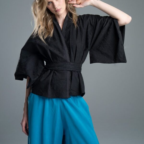 Modelka przodem prezentuje kimono Noda Black w ujęciu od kolan w górę, kimono jest związane, jedna ręka jest zgięta w łokciu i uniesiona, wyraźnie widać całe kimono oraz detal rękawa.