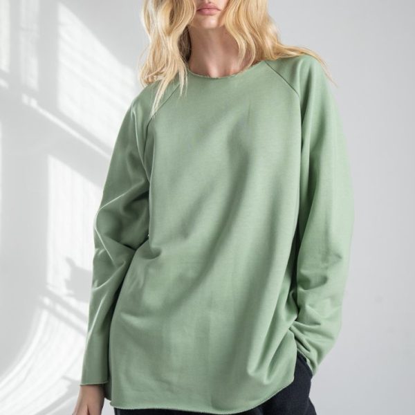 Bluza Mino Green delCane w miętowym odcieniu zieleni. Modelka przodem, widoczna od uda w górę, w swobodnej pozie, z jedną ręką w kieszeni spodni.
