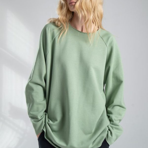 Bluza Mino Green delCane w miętowym odcieniu zieleni. Modelka widoczna od uda w górę, przodem, z rękami w kieszeniach spodni. Patrzy w bok.
