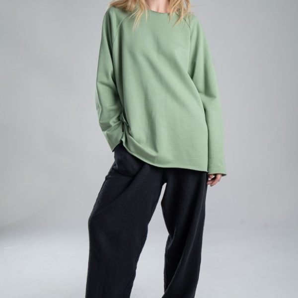 Bluza Mino Green delCane w miętowym odcieniu zieleni. Modelka przodem, w pełnej sylwetce, w swobodnej pozie, z jedną ręką w kieszeni spodni.