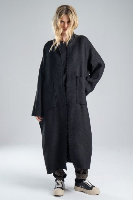 Cardigan Mino Black delCane w głębokim odcieniu czerni. Modelka przodem, w pełnej sylwetce, z jedną ręką opuszczoną wzdłuż ciała, a drugą ugiętą i cofniętą do tyłu. Wyraźnie widoczny cały przód cardiganu.