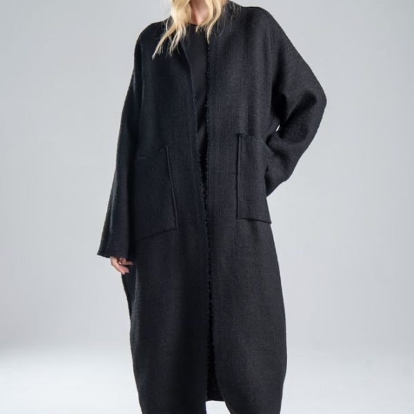 Cardigan Mino Black delCane w głębokim odcieniu czerni. Modelka przodem, w pełnej sylwetce, z jedną ręką opuszczoną wzdłuż ciała, a drugą ugiętą i cofniętą do tyłu. Wyraźnie widoczny cały przód cardiganu.
