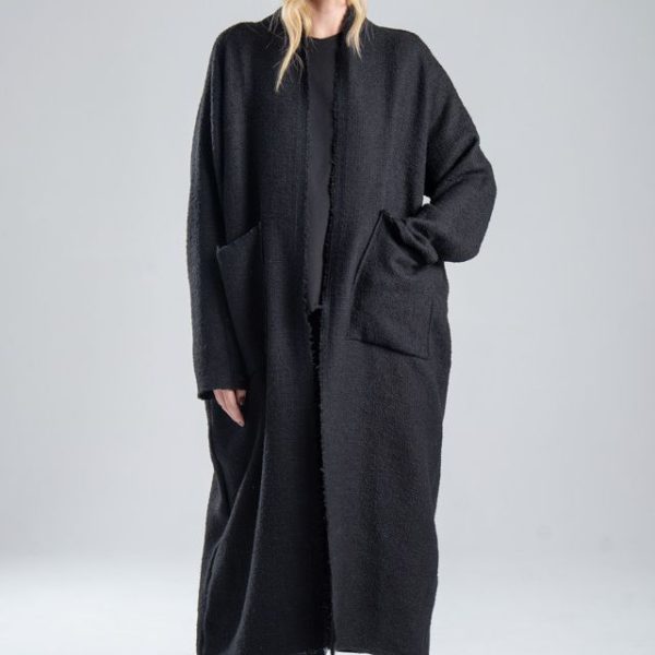 Cardigan Mino Black delCane w głębokim odcieniu czerni. Modelka przodem, w pełnej sylwetce, z jedną ręką w przedniej kieszeni cardiganu. Wyraźnie widoczny cały przód.