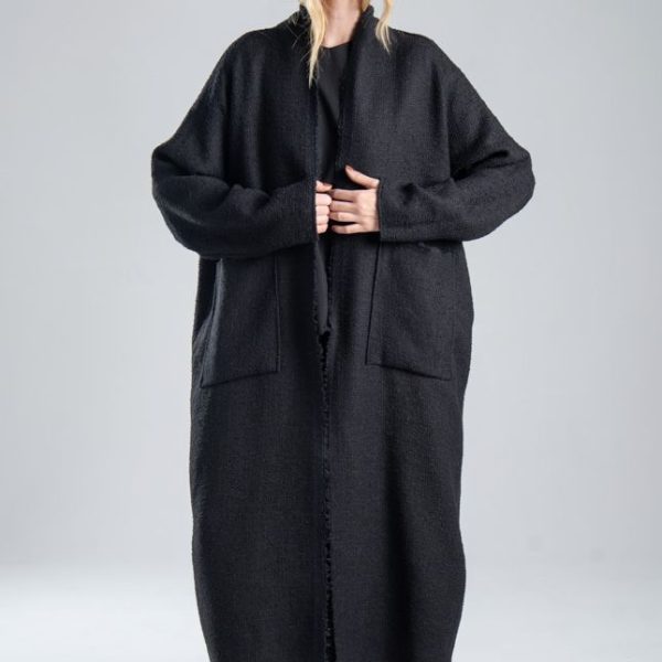 Cardigan Mino Black delCane w głębokim odcieniu czerni. Modelka przodem, w pełnej sylwetce, przytrzymuje obiema rękami przednie krawędzie cardiganu.
