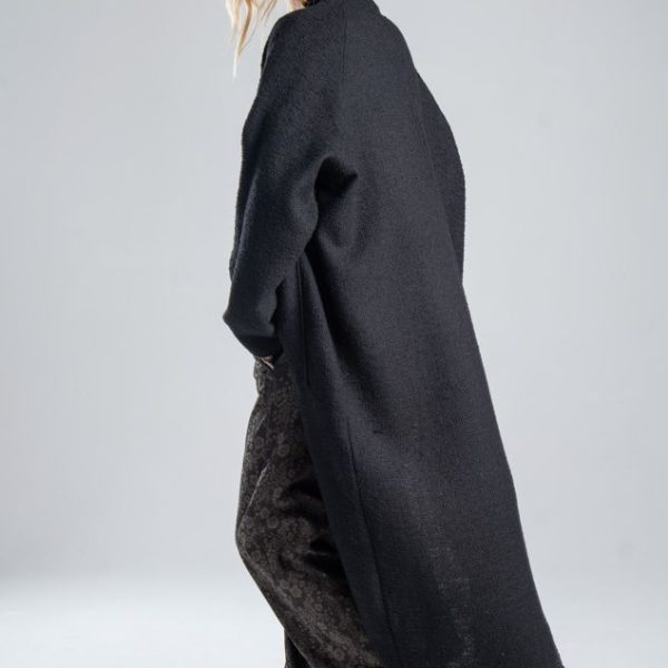 Cardigan Mino Black delCane w głębokim odcieniu czerni. Modelka ustawiona tyłem pod lekkim kątem, w ruchu, z jedną ręką w kieszeni spodni. Widoczny bok i tył cardiganu.