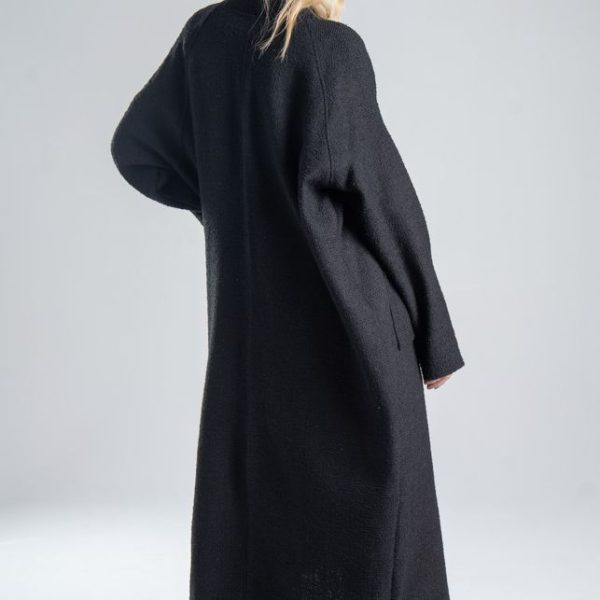 Cardigan Mino Black delCane w głębokim odcieniu czerni. Modelka ustawiona tyłem pod lekkim kątem, w ruchu, jakby szła do przodu. Widoczny tył, bok i fragment przodu cardiganu.