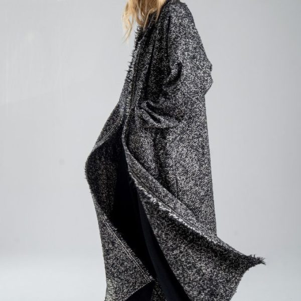 Cardigan Mino Wool delCane w czarno-białym melanżu. Modelka ustawiona bokiem, w pełnej sylwetce, w ruchu, z rękami w kieszeniach. Wyraźnie widoczny bok cardiganu.