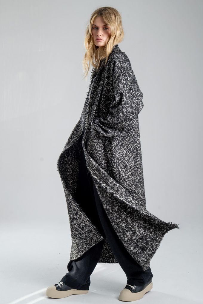 Cardigan Mino Wool delCane w czarno-białym melanżu. Modelka ustawiona bokiem, w pełnej sylwetce, w ruchu, z rękami w kieszeniach. Wyraźnie widoczny bok cardiganu.