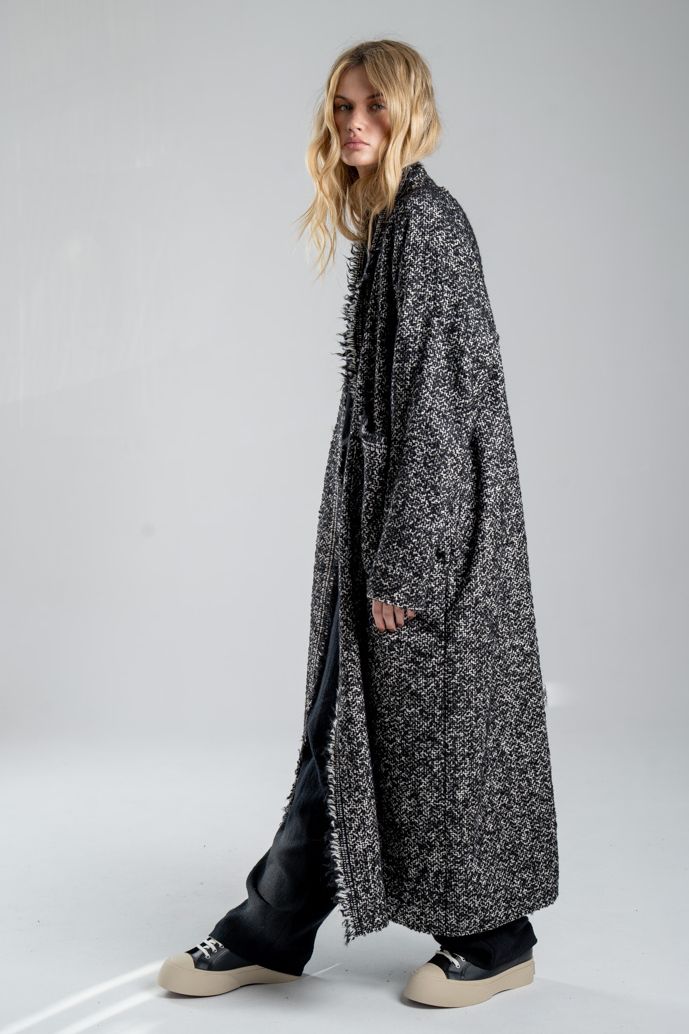 Cardigan Mino Wool delCane w czarno-białym melanżu. Modelka ustawiona bokiem, w pełnej sylwetce, z rękami opuszczonymi wzdłuż ciała, patrzy w obiektyw.