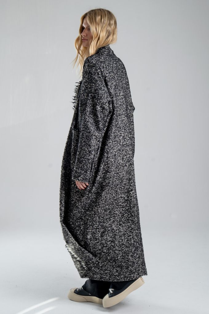 Cardigan Mino Wool delCane w czarno-białym melanżu. Modelka w pełnej sylwetce, ustawiona tyłem pod lekkim kątem, w pozie sugerującej ruch. Widoczny bok i fragment tyłu cardiganu.