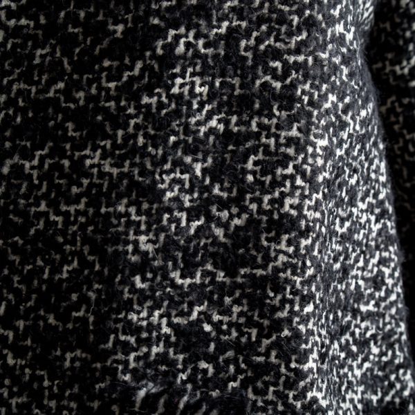 Zbliżenie na wełnę cardiganu Mino Wool delCane. Wyraźnie widoczny czarno-biały melanż, faktura materiału oraz oryginalne wykończenie kieszeni krótkimi frędzlami.