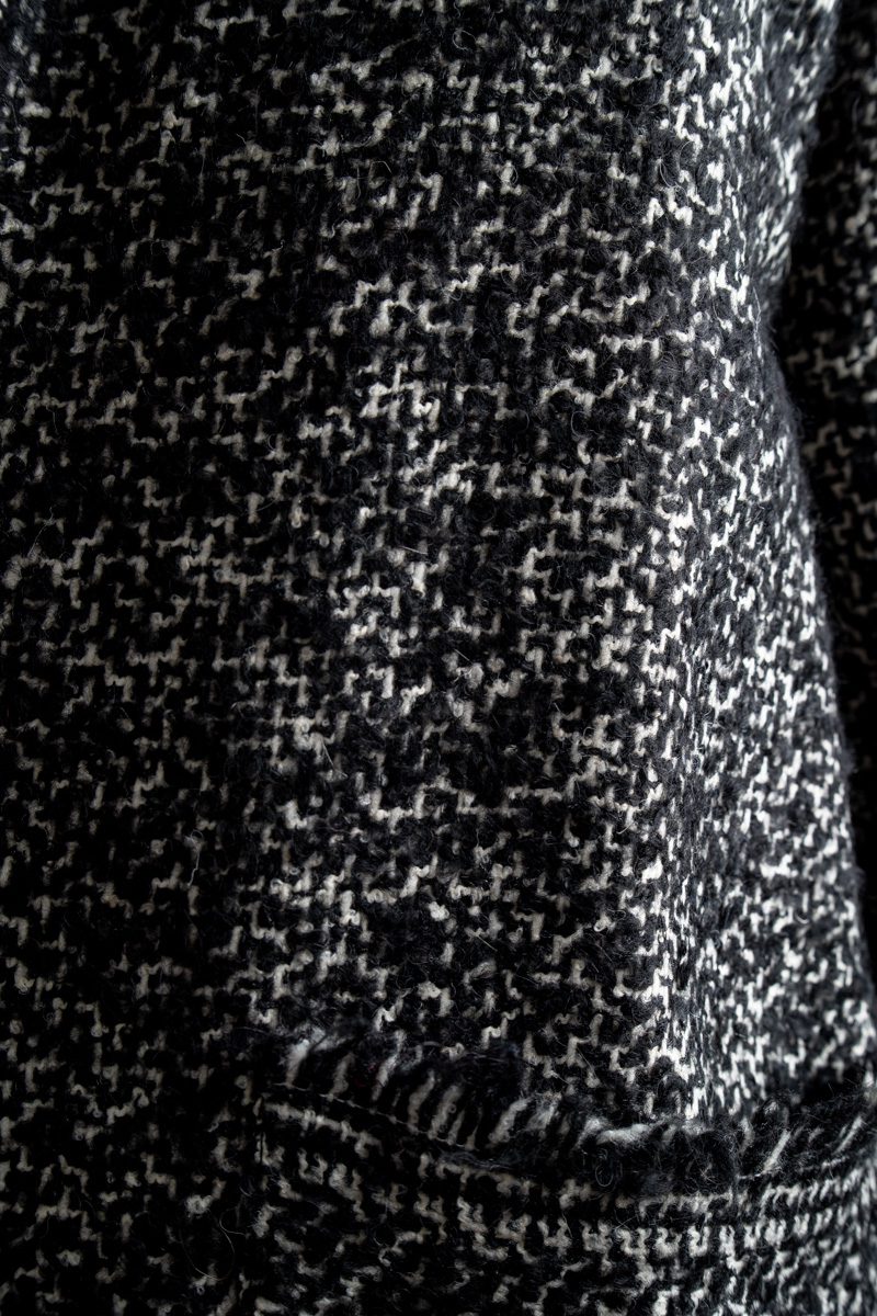 Zbliżenie na wełnę cardiganu Mino Wool delCane. Wyraźnie widoczny czarno-biały melanż, faktura materiału oraz oryginalne wykończenie kieszeni krótkimi frędzlami.