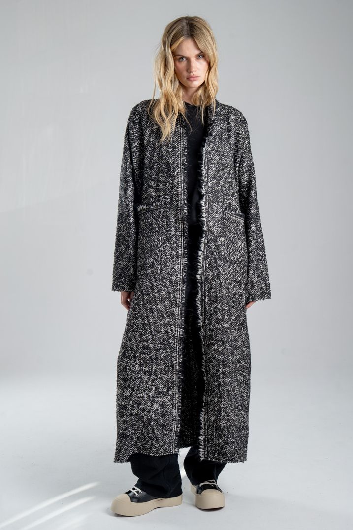 Cardigan Mino Wool delCane w czarno-białym melanżu. Modelka przodem, w pełnej sylwetce, z rękami opuszczonymi wzdłuż ciała. Wyraźnie widoczny przód cardiganu.