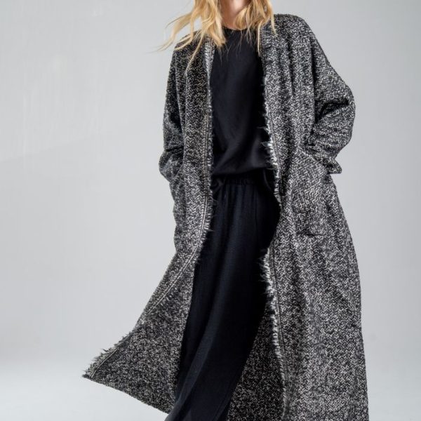 Cardigan Mino Wool delCane w czarno-białym melanżu. Modelka przodem, w pełnej sylwetce, w ruchu, z rękami w kieszeniach cardiganu. Wyraźnie widoczny cały przód.