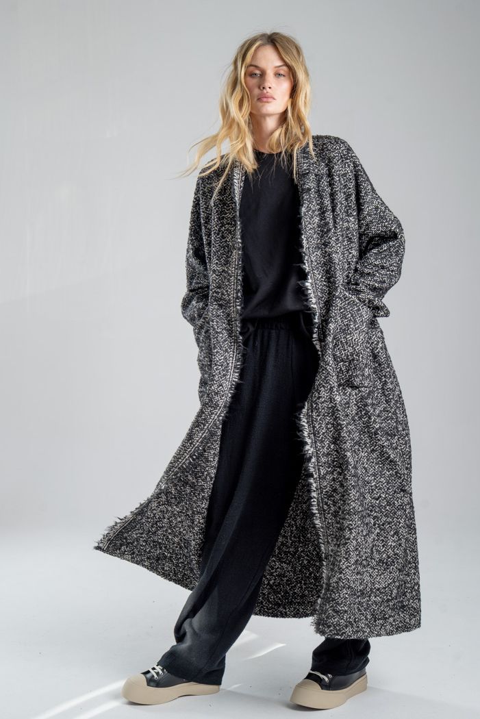 Cardigan Mino Wool delCane w czarno-białym melanżu. Modelka przodem, w pełnej sylwetce, w ruchu, z rękami w kieszeniach cardiganu. Wyraźnie widoczny cały przód.