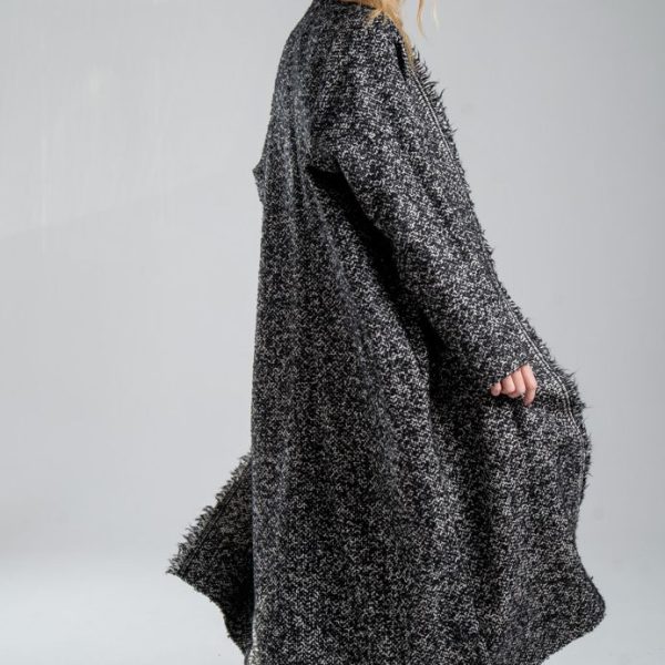 Cardigan Mino Wool delCane w czarno-białym melanżu. Modelka ustawiona tyło-bokiem, w ruchu. Widoczny bok i tył cardiganu.