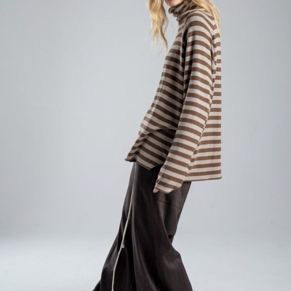 Sweter z golfem Mino Stripes delCane w beżowo-brązowe paski. Modelka w pełnej sylwetce, ustawiona bokiem, lekko odchylona do tyłu, z rękami opuszczonymi wzdłuż ciała.