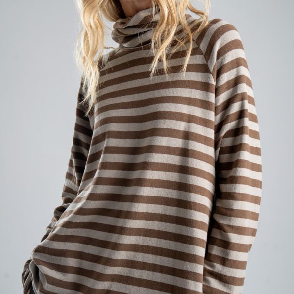 Sweter z golfem Mino Stripes delCane w beżowo-brązowe paski. Zbliżenie na przód swetra, modelka widoczna od ud w górę, z sylwetką lekko skręconą w bok i rękami w kieszeniach spodni.